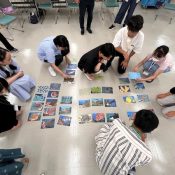 ７名の学生が床に生き物カードを並べて学習している様子